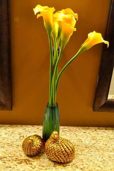 A vase filled with yellow flowers and two gold birds on a table.