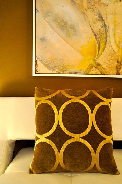 A brown and gold pillow is sitting on a bed under a painting