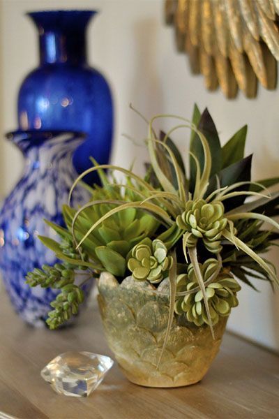 A vase filled with green plants sits on a table next to two blue vases