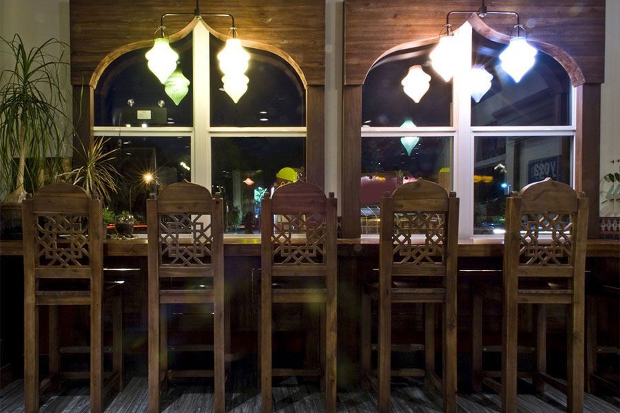 A row of wooden chairs are lined up in front of a window in a restaurant.
