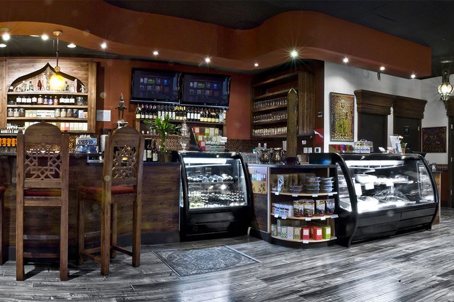 A restaurant with a bar , chairs , display cases and shelves.
