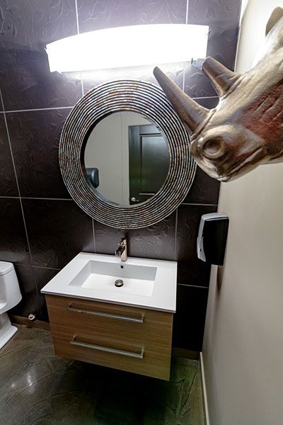 A bathroom with a sink a mirror and a rhino head on the wall