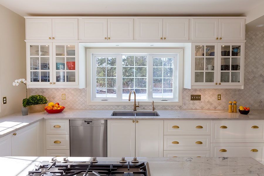 A kitchen with white cabinets , a stove , a sink and a window.