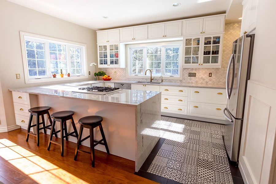 A kitchen with white cabinets , granite counter tops , stools and a large island.