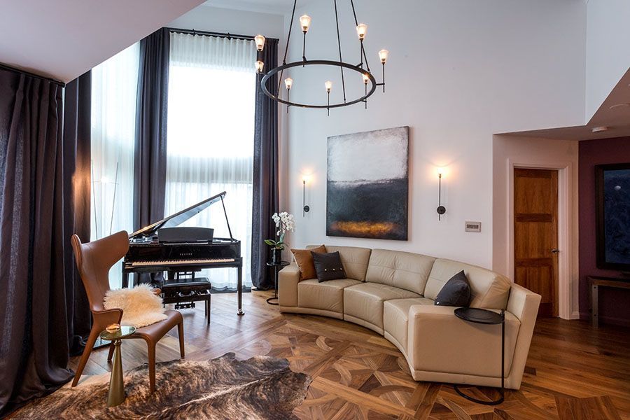 A living room with a couch , chair , piano and chandelier.