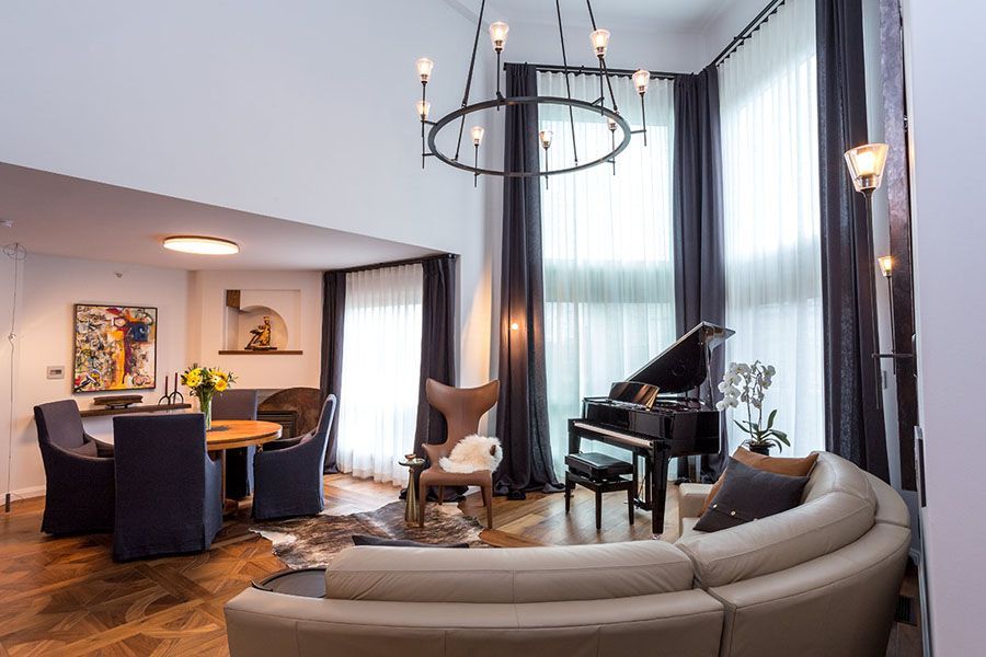 A living room with a couch , chairs , a piano and a chandelier.