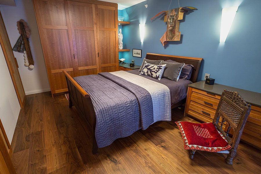 A bedroom with a bed , chair , nightstand and dresser.