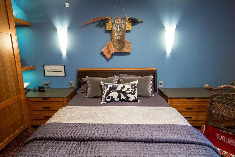 A bedroom with a bed , two nightstands and a painting on the wall above the bed.