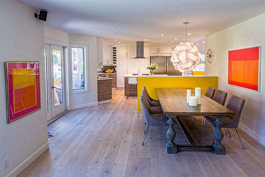 A dining room with a table and chairs and a kitchen in the background