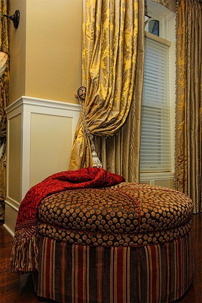 A striped ottoman with a red blanket on it is in a living room next to a window.