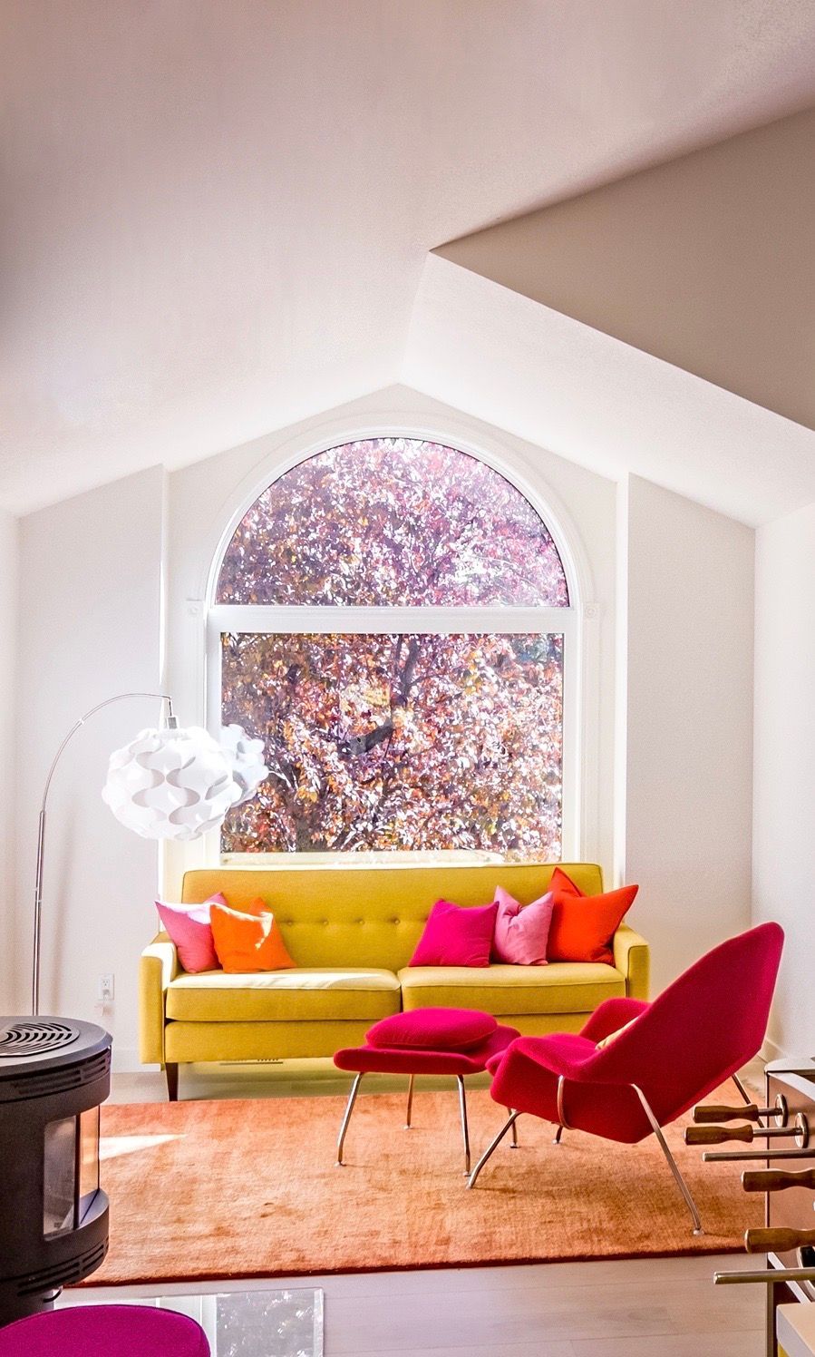 Modern living room with colorful chairs, fireplace, bright window, and fruit bowl on a counter