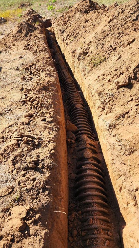 A large pipe is laying in the dirt in a trench.
