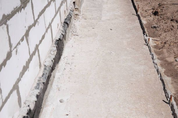 Concrete pathway next to a cinder block wall, with dirt on one side.