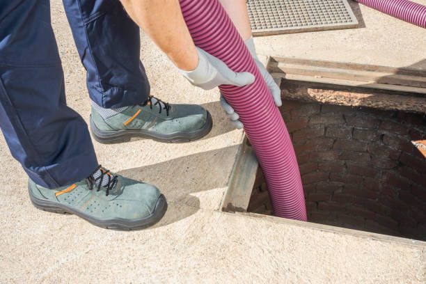 Person in work boots holding a pink hose, inserting it into an open brick manhole.