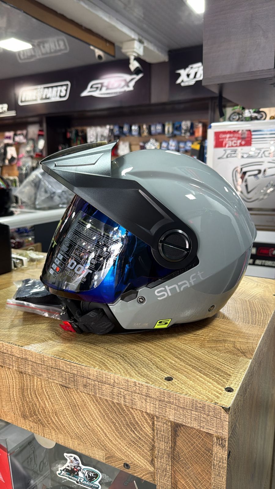 Casco de motocicleta gris con visera azul en expositor de madera.