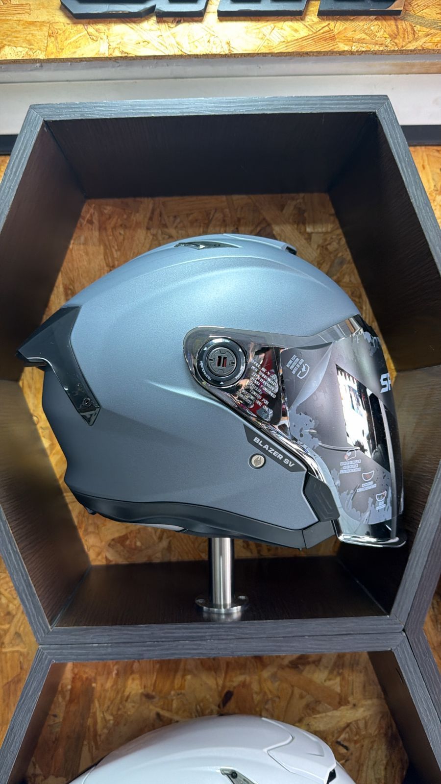 Casco de motocicleta gris con visera cromada exhibido en un estante de madera.