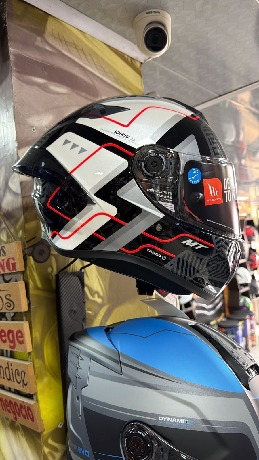 Casco de motocicleta: diseño en negro, blanco y rojo en exhibición, con un casco azul y gris debajo.