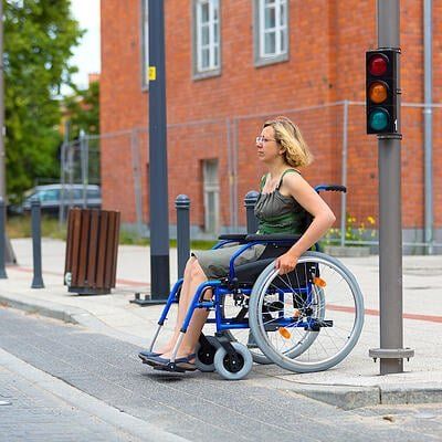 a woman in a wheelchair is waiting at a traffic light.