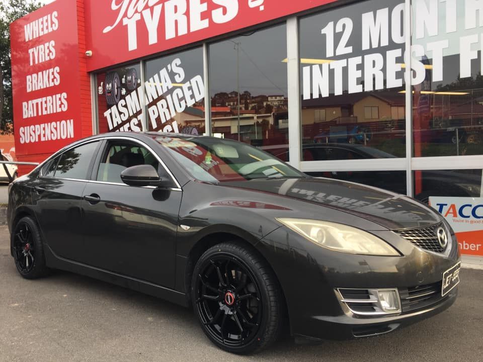 Dark gray Mazda sedan parked outside a tire shop with a red sign.