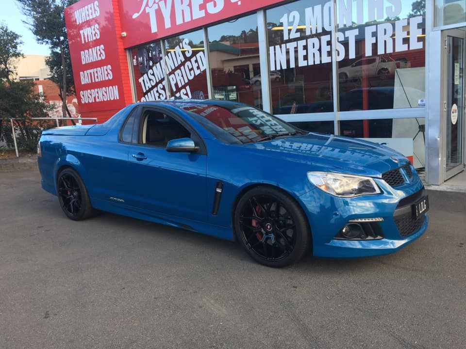 Blue Holden utility vehicle parked in front of a tire shop with black rims.