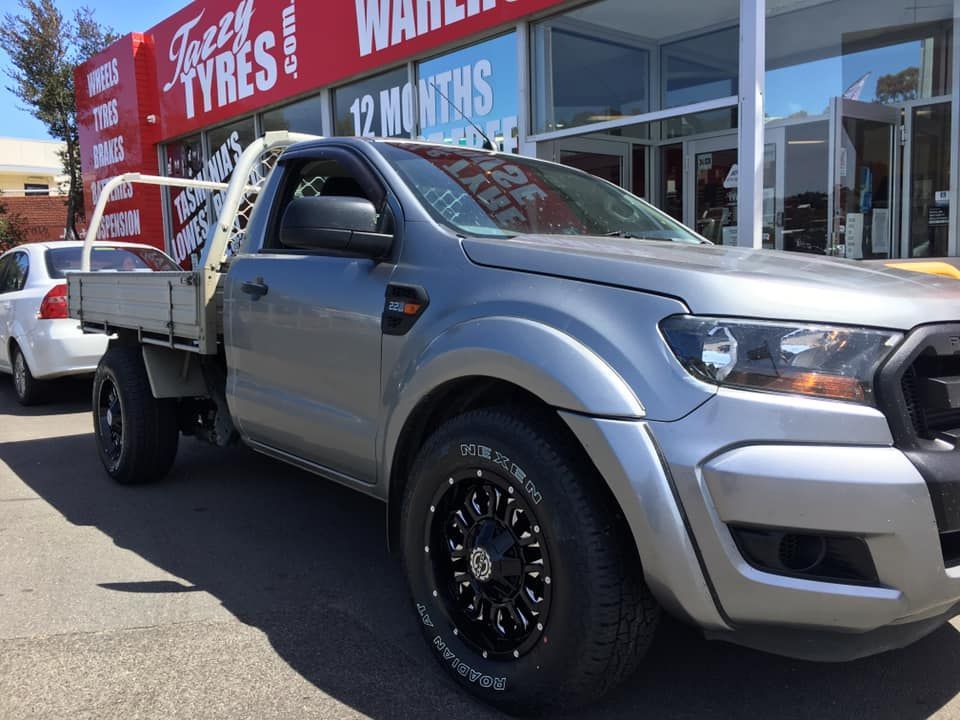 Gray Ford pickup truck with black wheels parked in front of a tire shop.