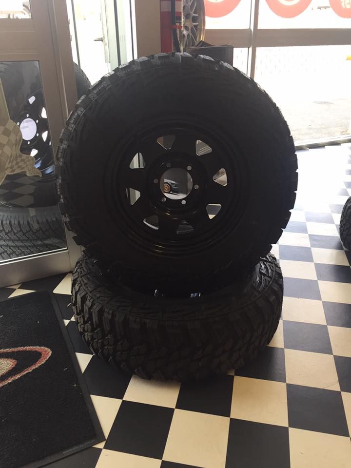 Two black off-road tires and rims stacked on a checkered floor inside a tire shop.