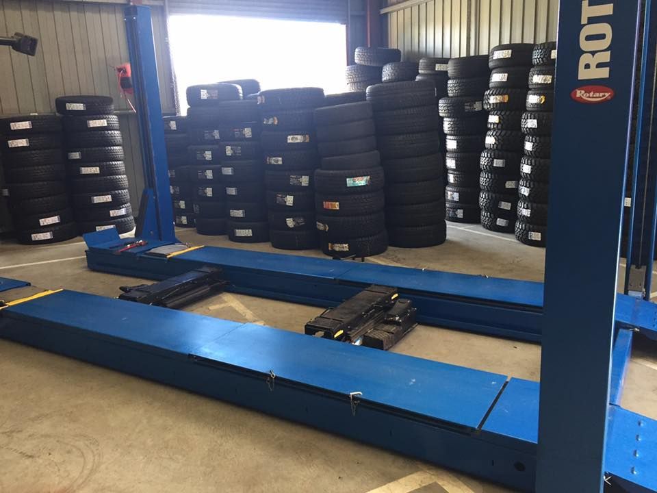 Blue car lift in a tire shop with stacks of tires in the background.