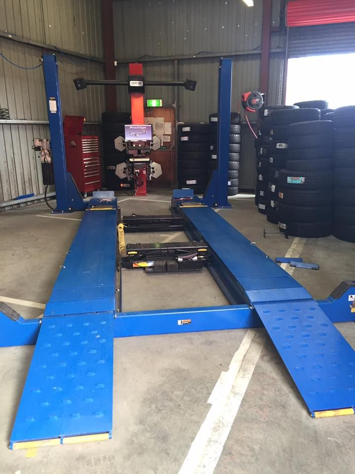 Blue car lift in a workshop, with alignment equipment in the background and tires stacked.