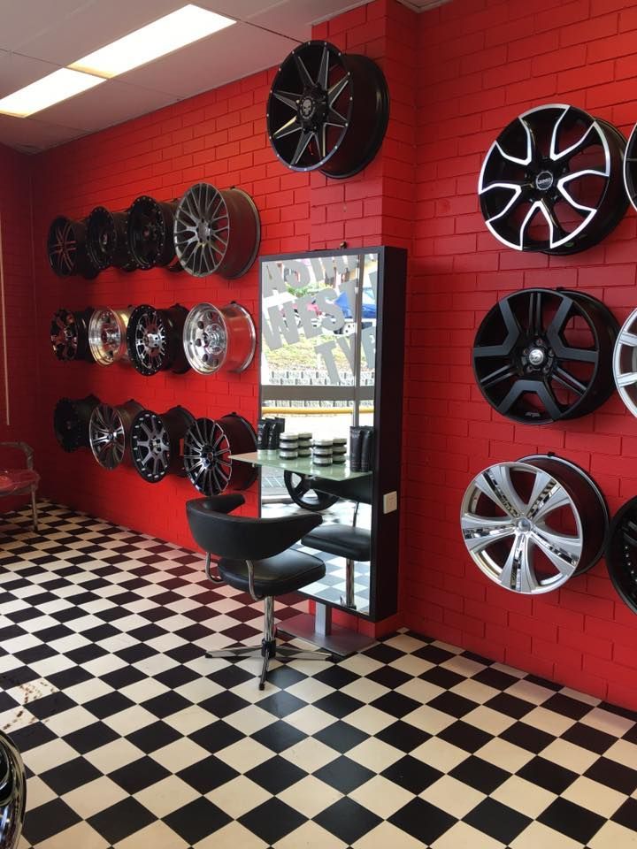 A tire shop interior with red brick walls displaying various rims. Black and white checkered floor, chair, and mirror.