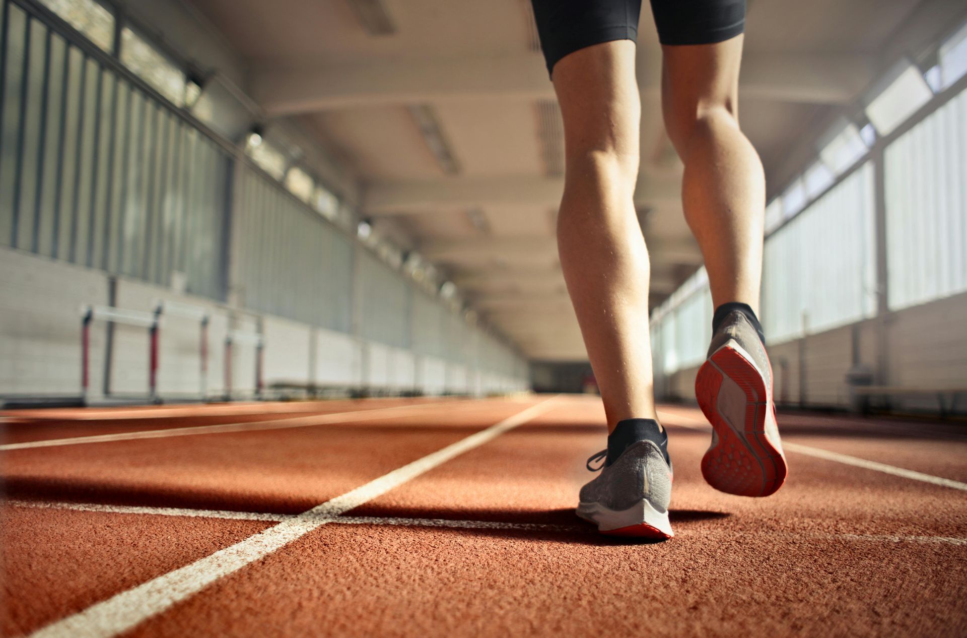 Person running on a red track indoors, focused on their legs and feet, with gray shoes.