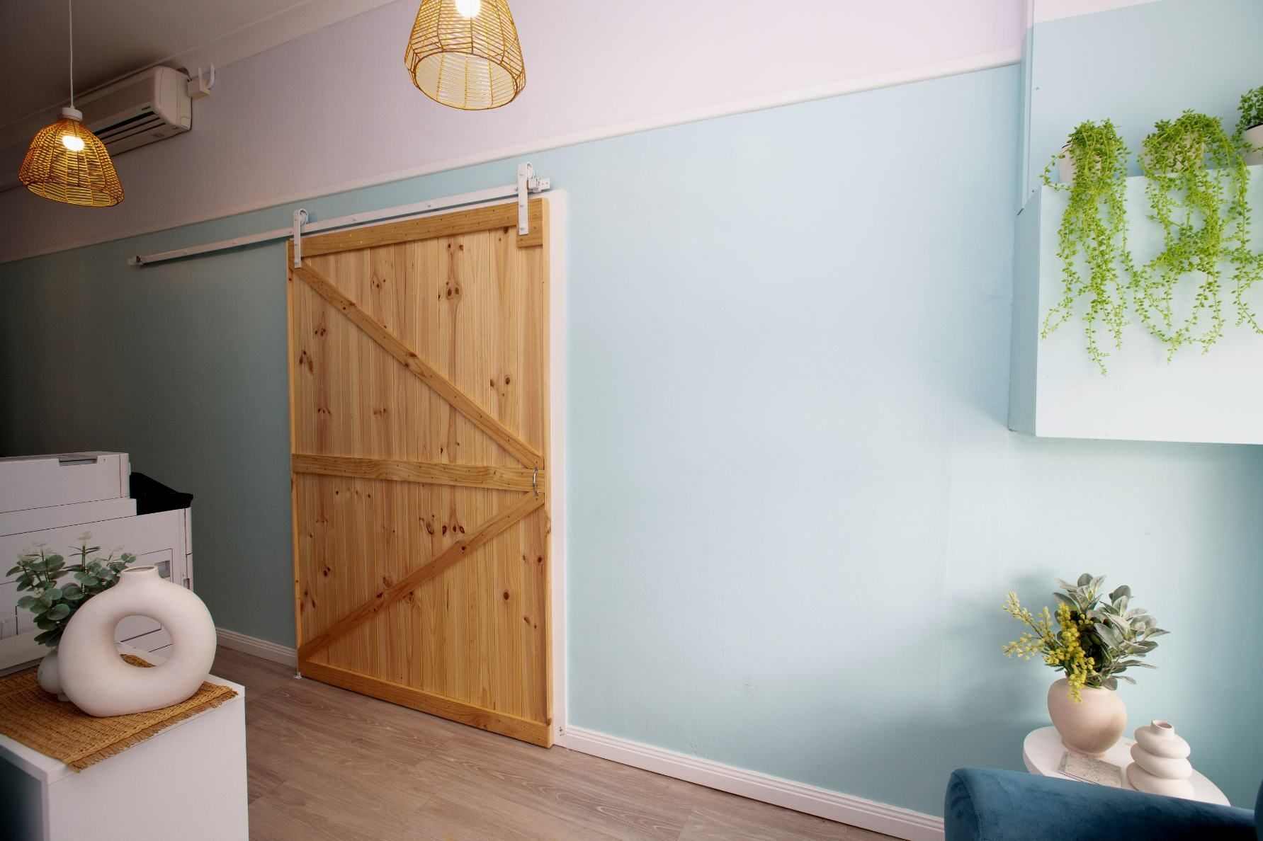 Wooden Barn Door on a Light Blue Wall, With Hanging Plants and Decor in a Room With Natural Light — Daly Legal In Macksville, NSW