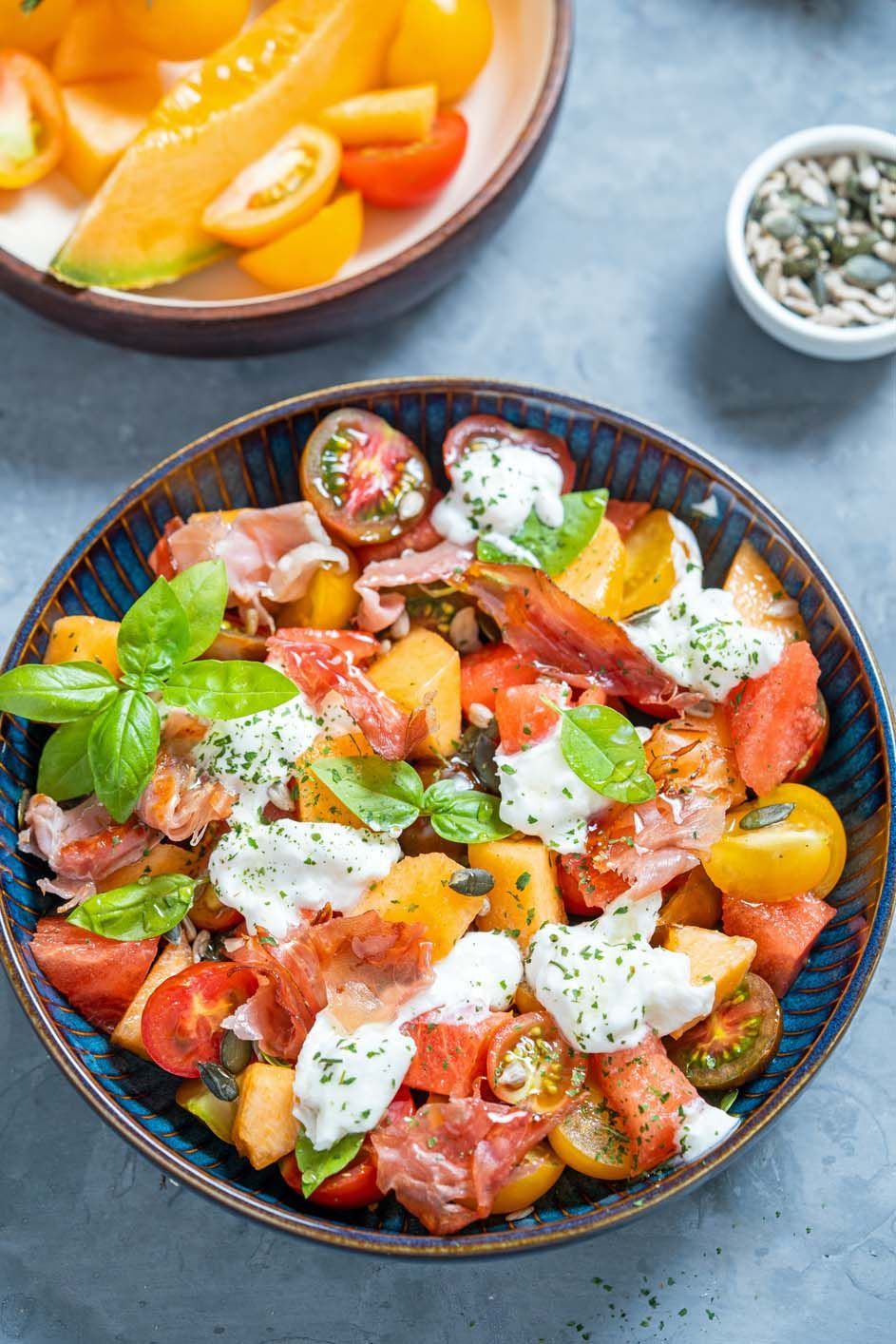 A salad with tomatoes, melon, prosciutto and basil in a bowl