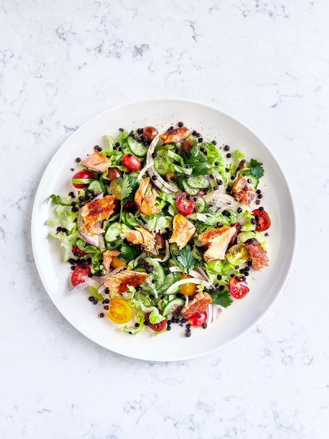 A white plate topped with a salad of vegetables and meat on a table