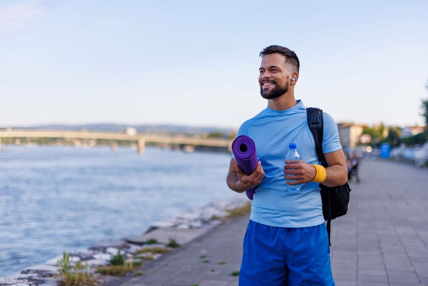 A man is holding a yoga mat and a bottle of water