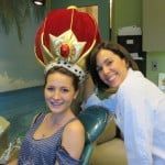 Two smiling people in costumes pose together indoors, one wearing a red-and-gold crown headpiece.