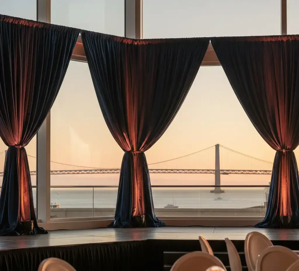 Navy blue draped curtains framing a view of a bridge and water at sunset.