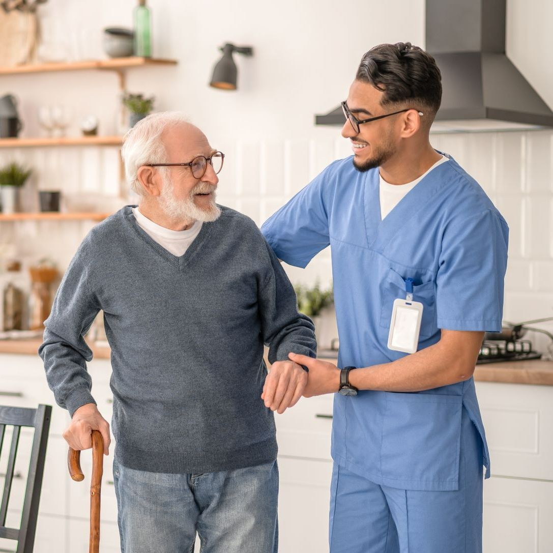 A Nurse Is Helping An Elderly Man Walk With A Cane