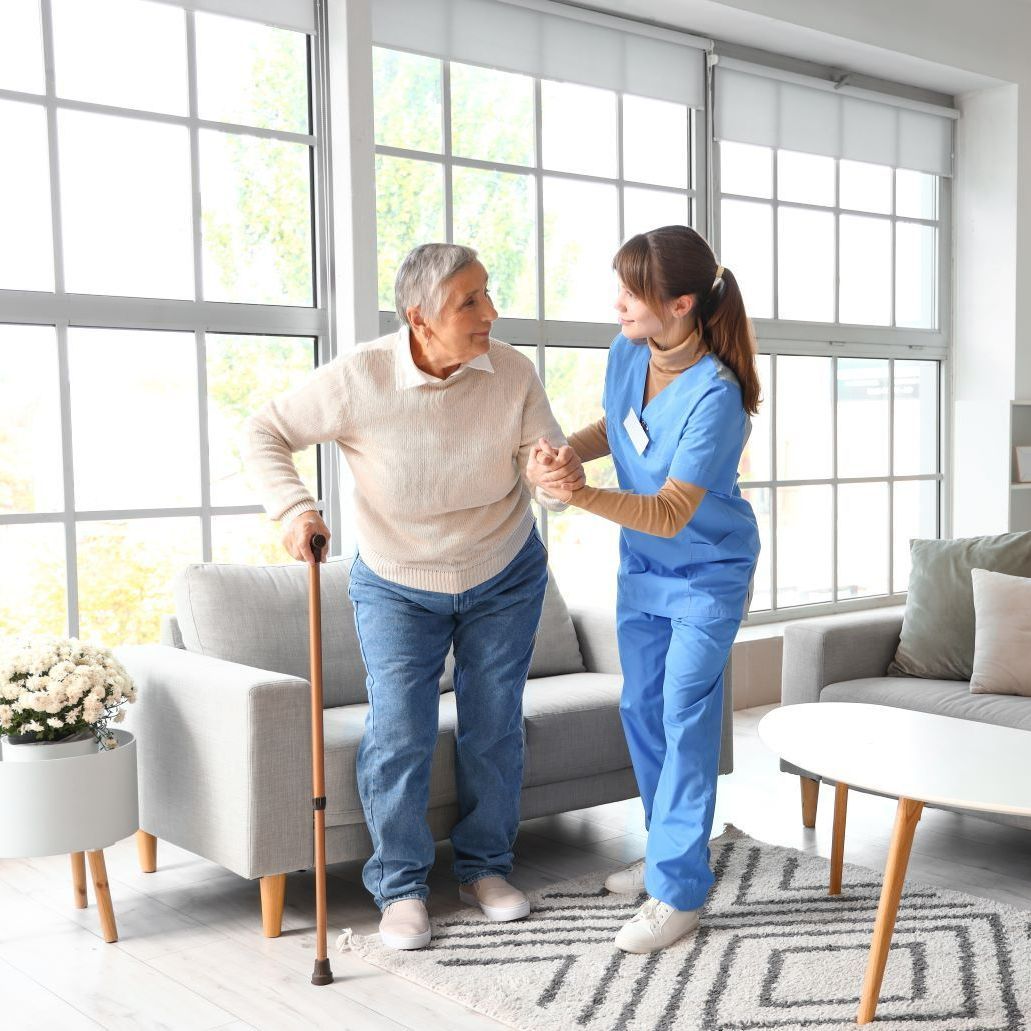 A Nurse Is Helping An Elderly Woman Walk In A Living Room