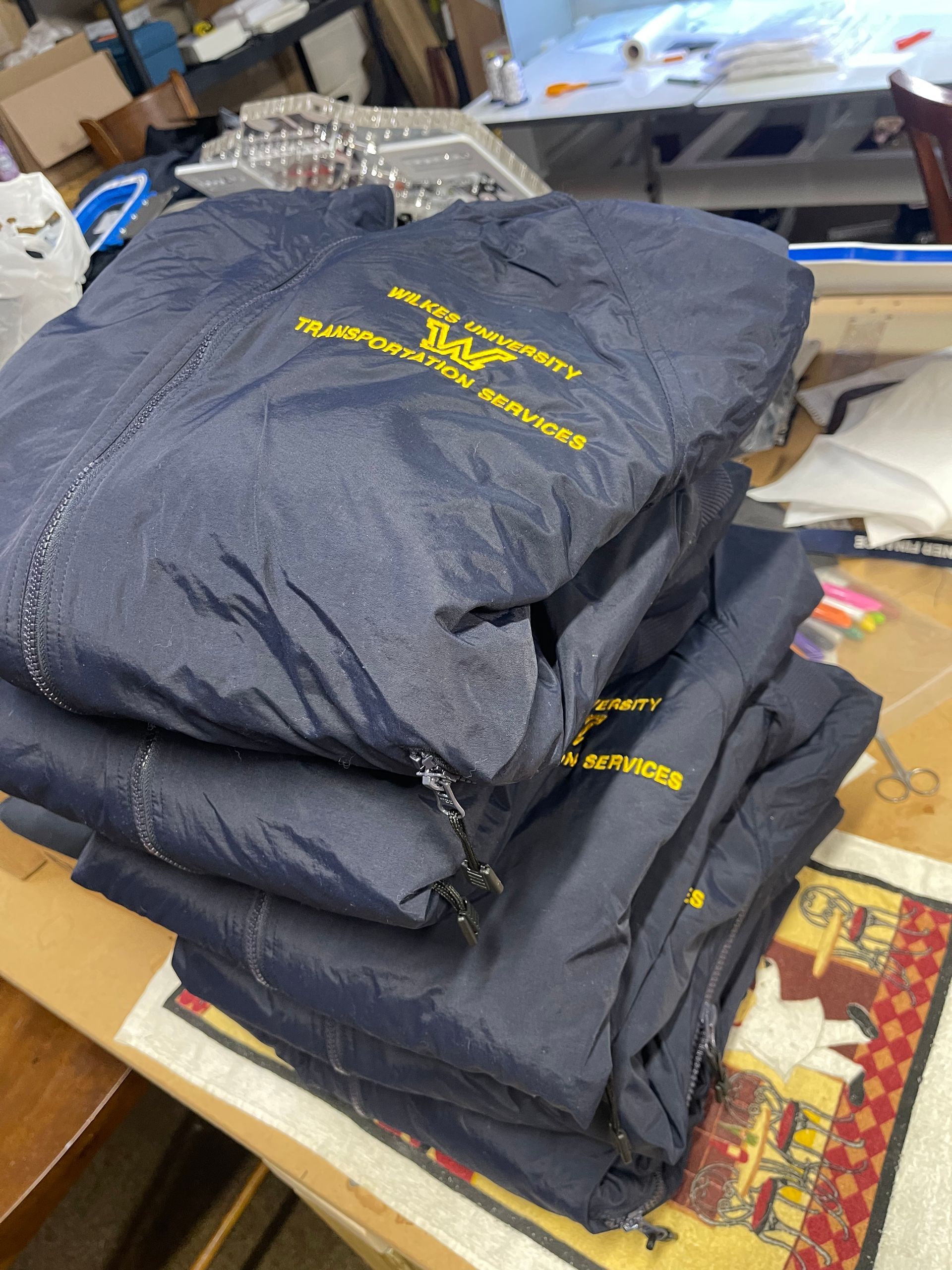 A stack of navy blue jackets with yellow embroidery, resting on a table in an office or workspace setting.