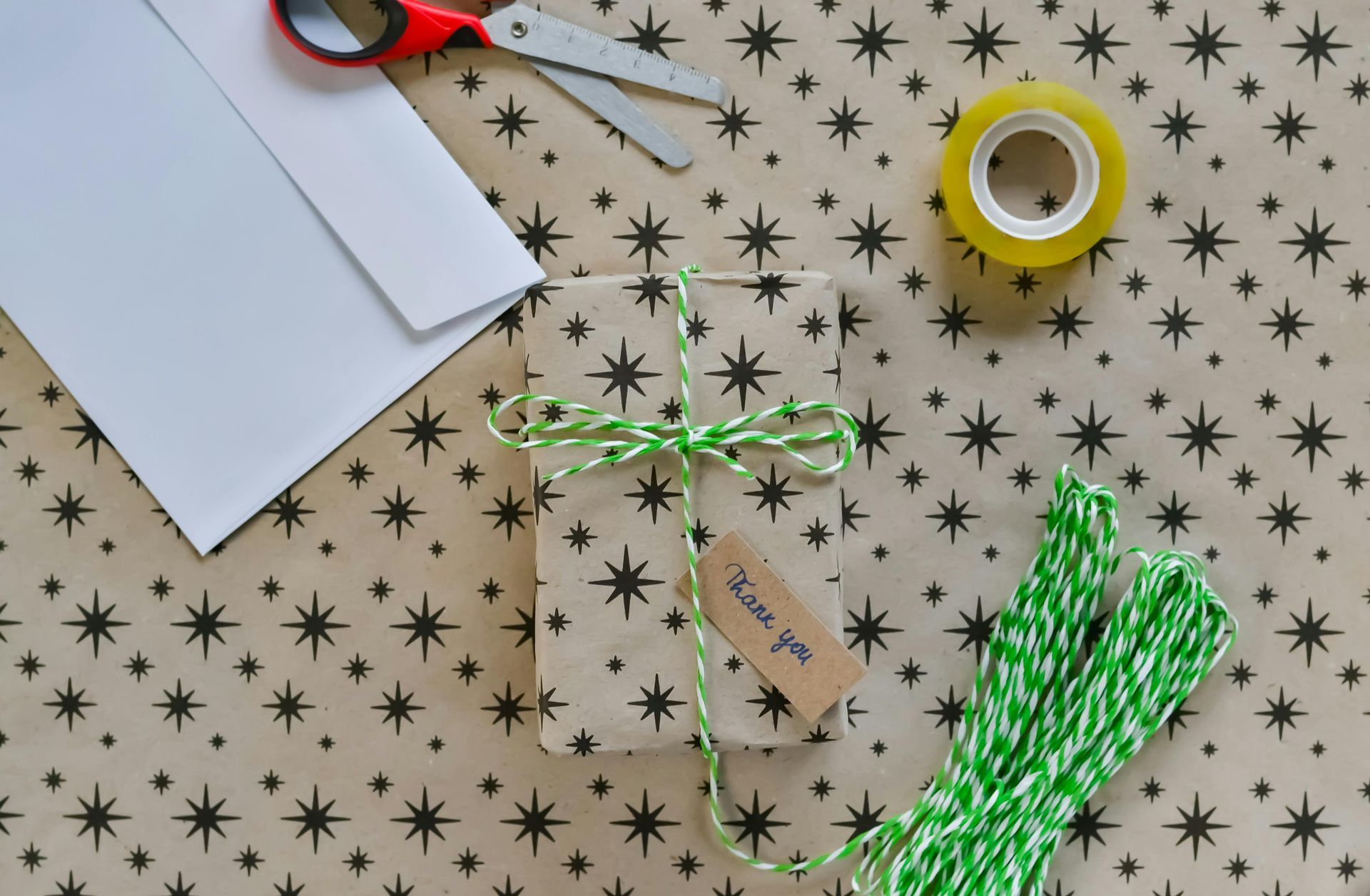 A gift wrapped in star-patterned paper, tied with green twine, sitting on matching paper with scissors and tape.