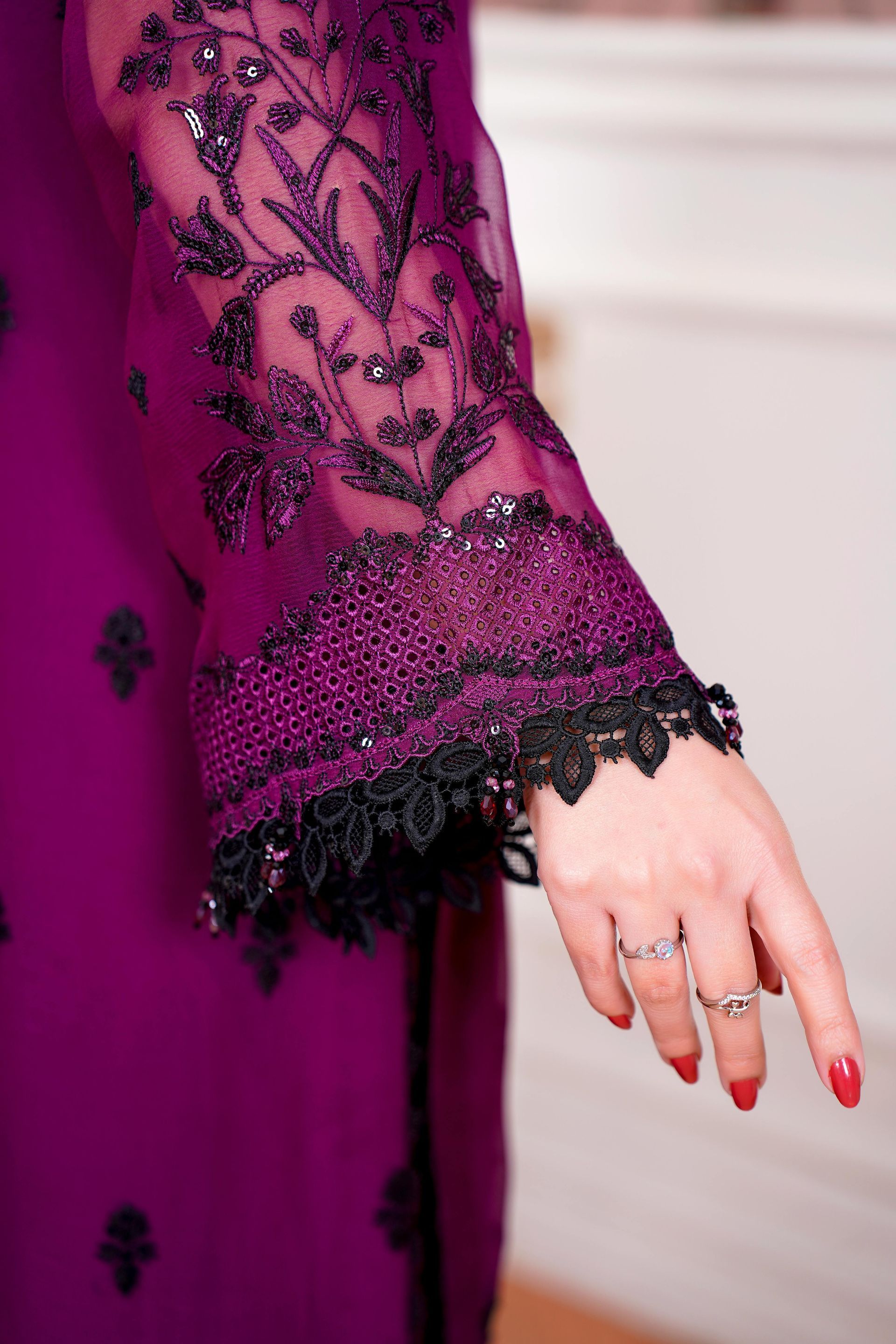 A close-up of a vibrant purple sleeve with intricate black embroidery and a scalloped lace edge, worn with silver rings.