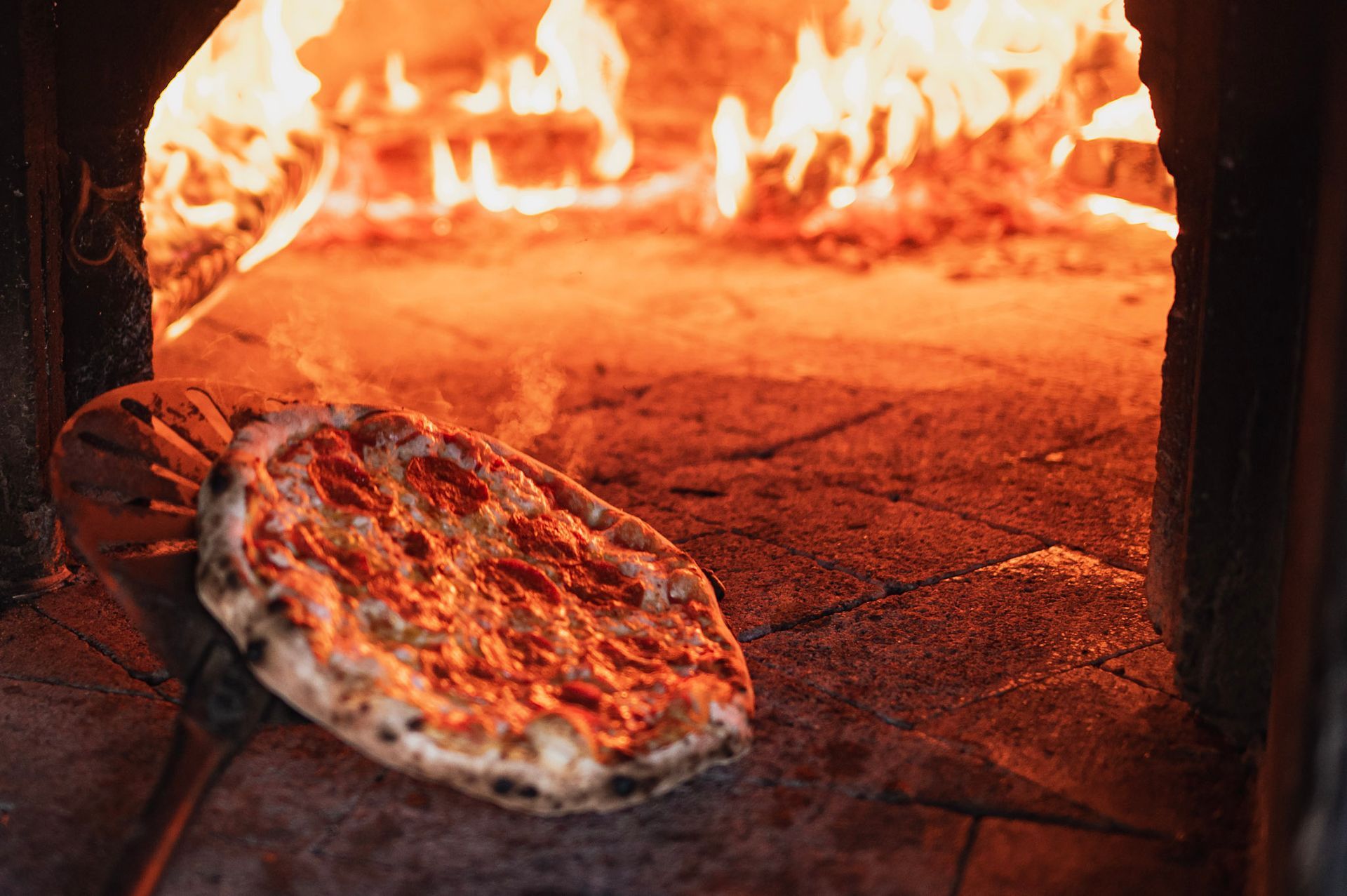 A pizza is being cooked in an oven with flames coming out of it.