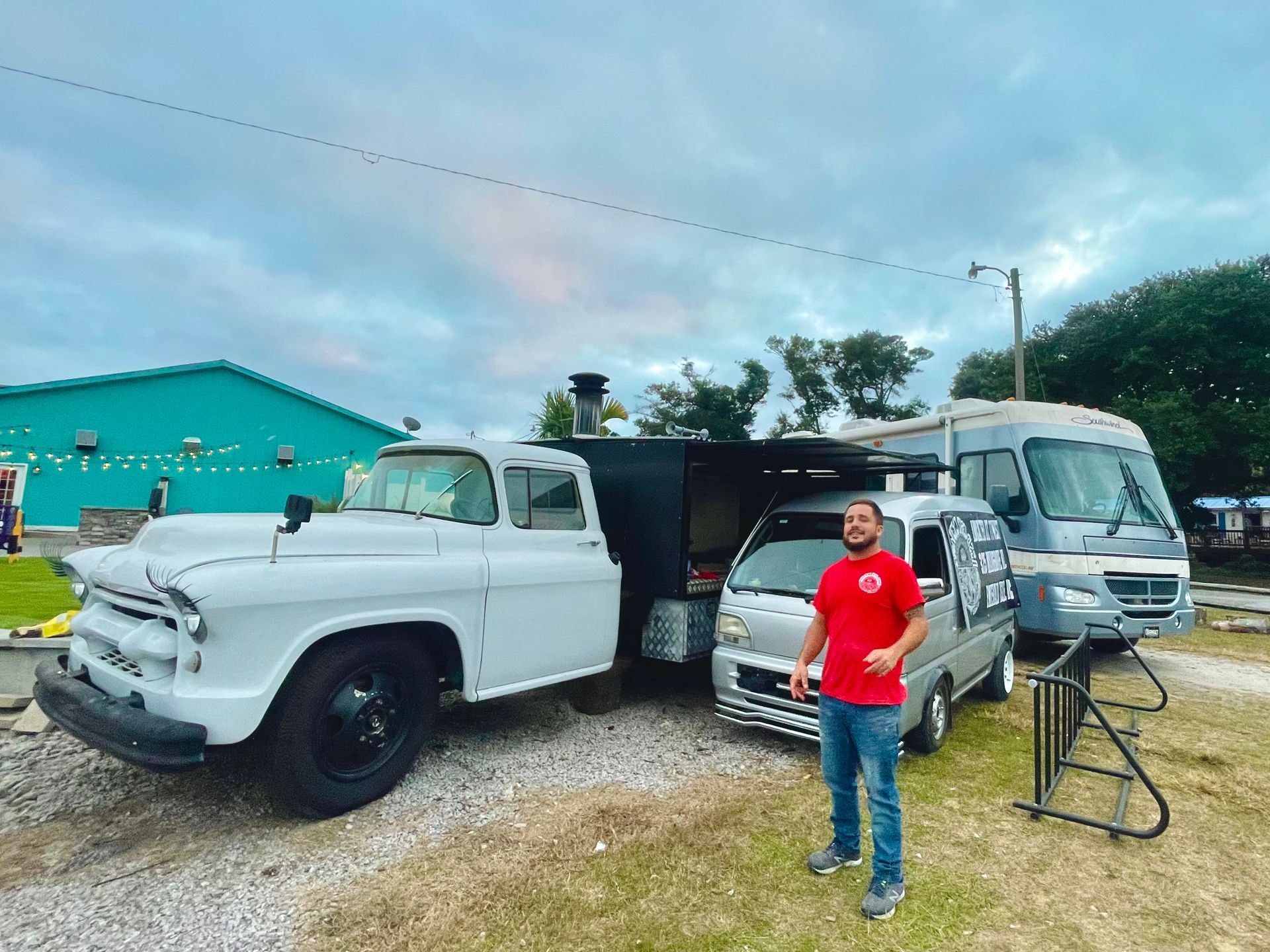 A man in a red shirt is standing in front of a white truck.