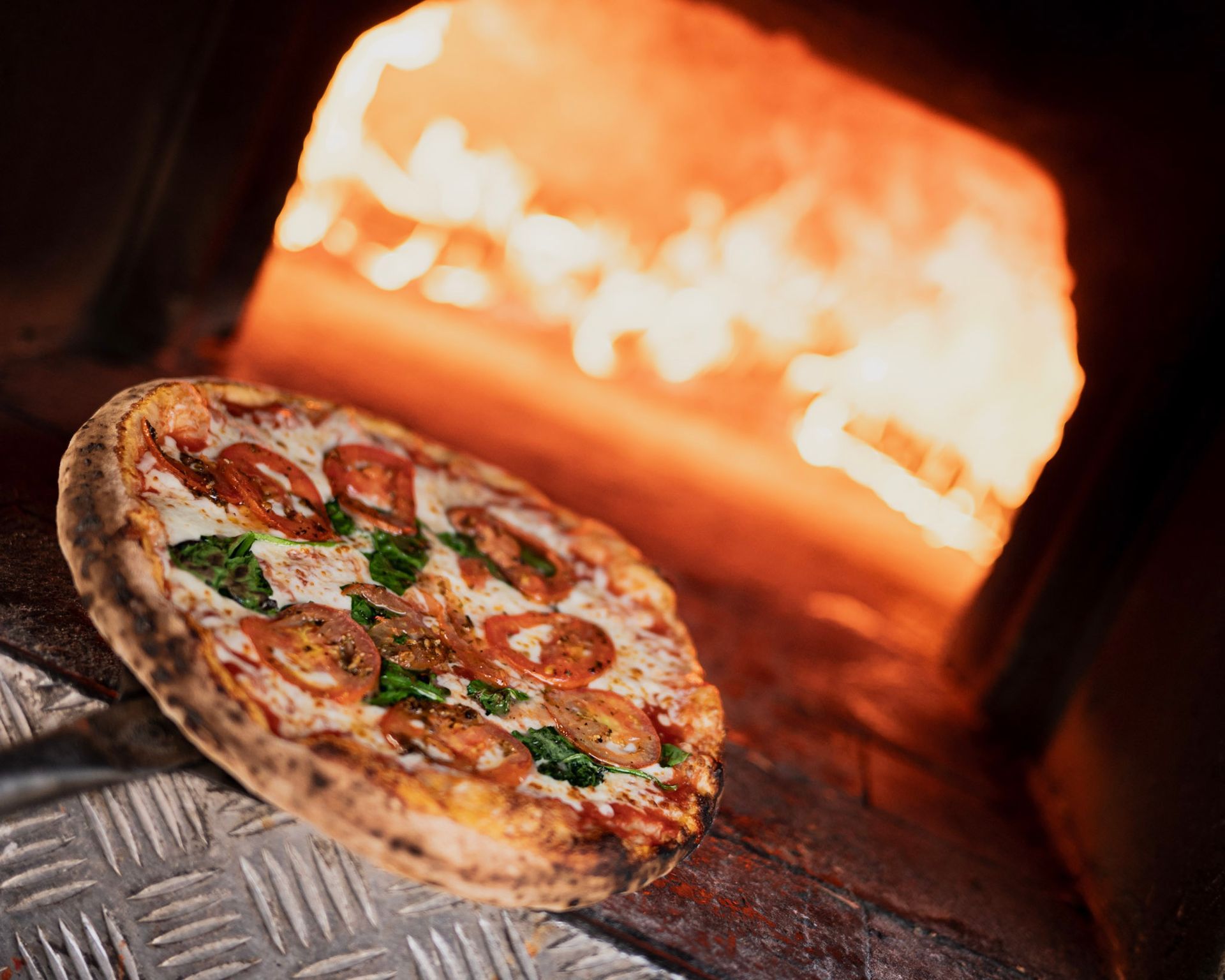 A pizza is sitting in front of a wood fired oven.
