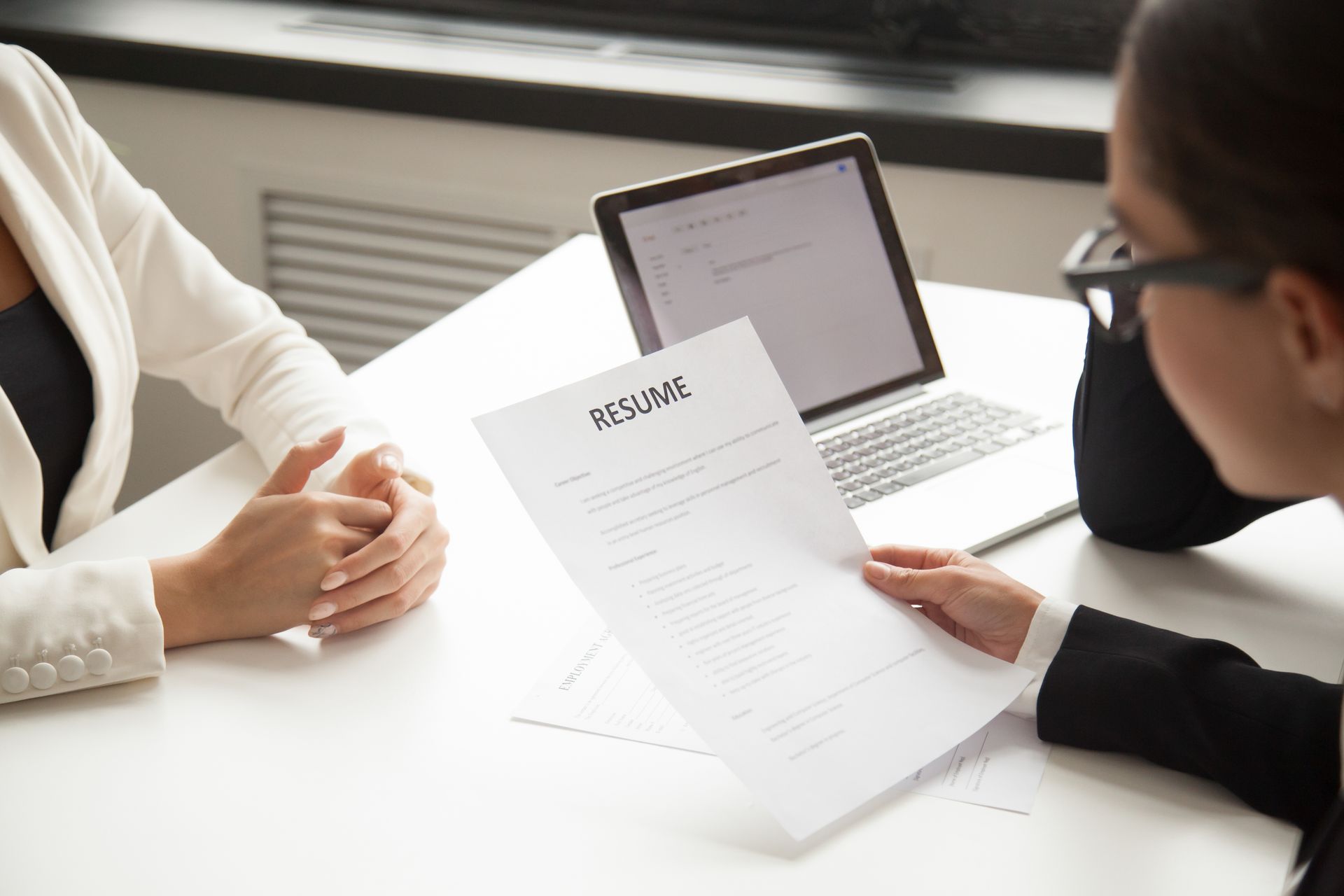 two women are sitting at a table with a laptop and a resume .