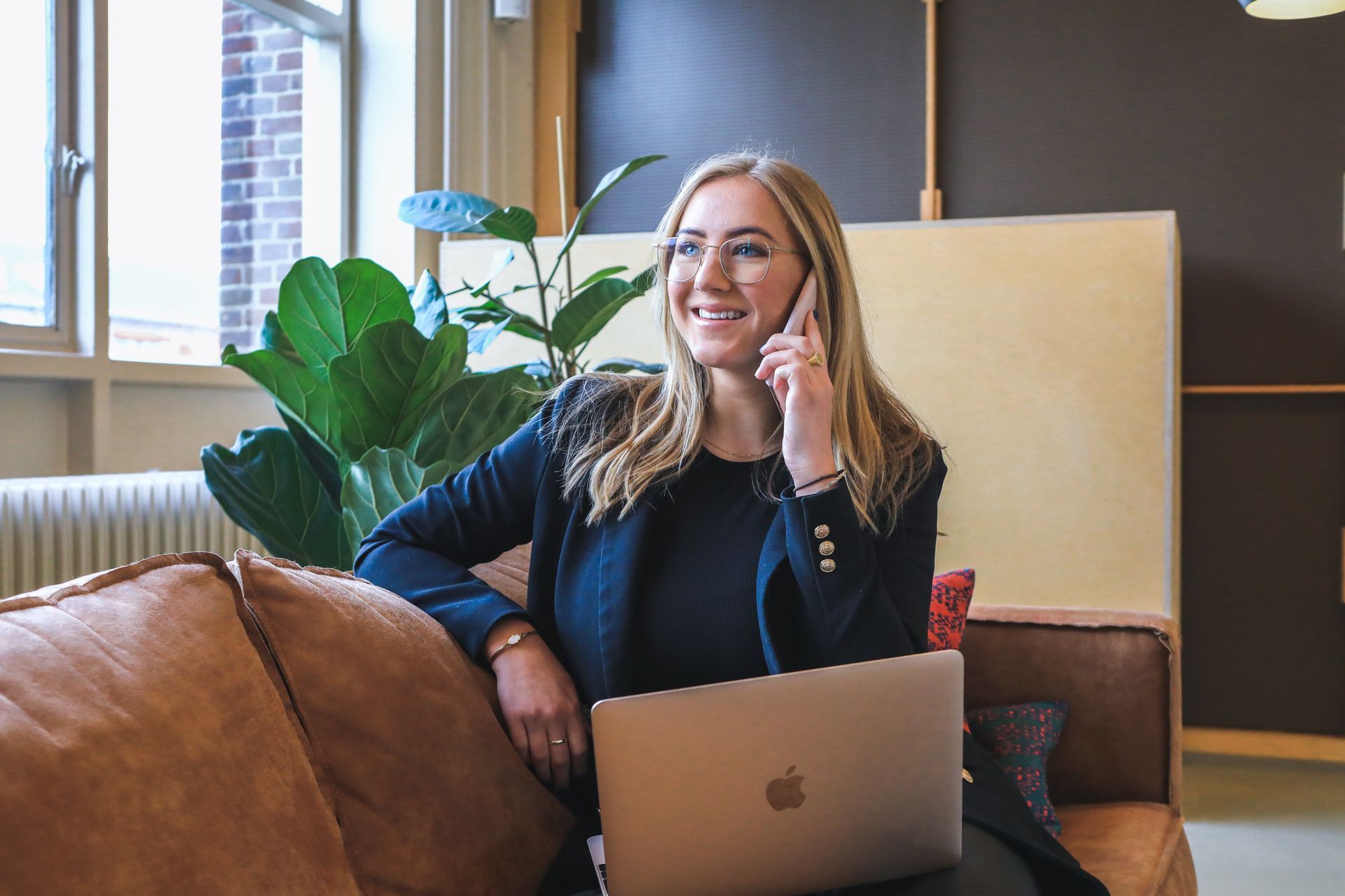a woman is sitting on a couch with a laptop and talking on a cell phone .