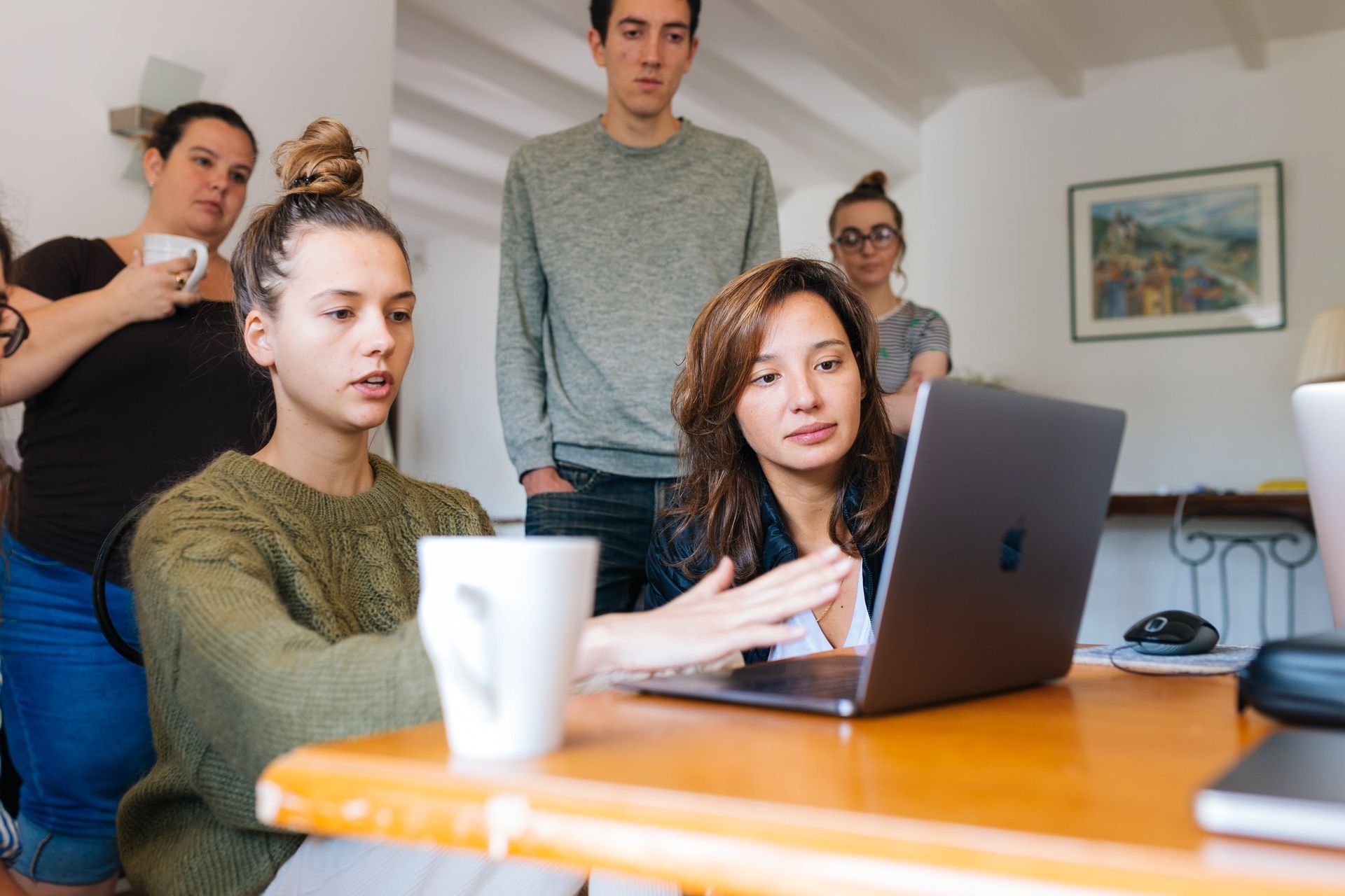a group of people are sitting around a table looking at a laptop computer .