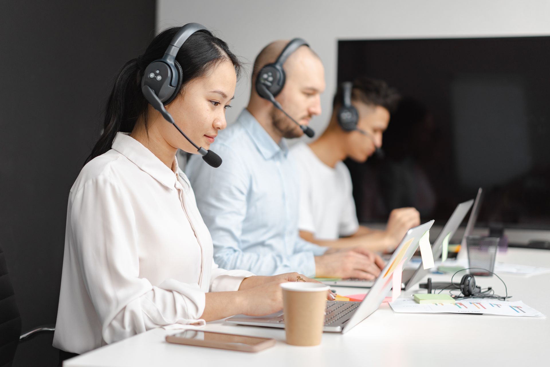 a group of people wearing headsets are sitting at a table with laptops .