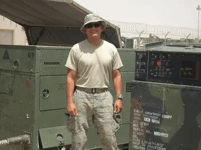 A man in a military uniform is standing in front of a military vehicle.
