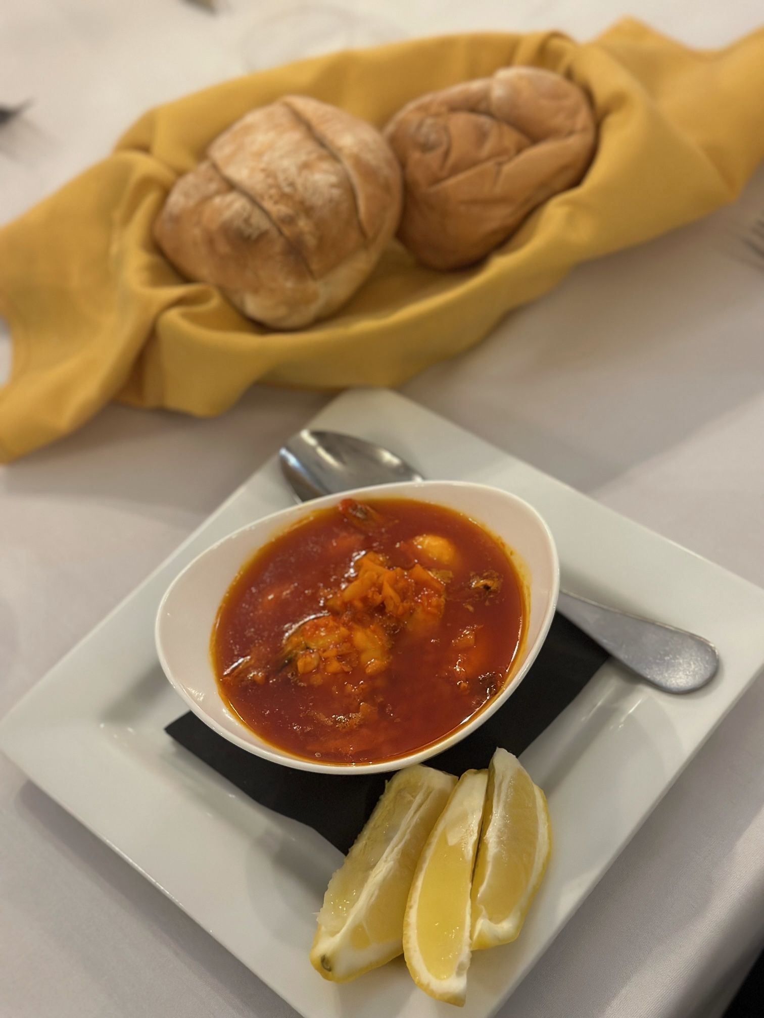 A bowl of soup next to a basket of bread